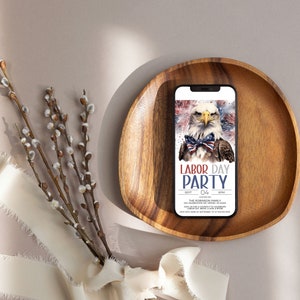 May include: A wooden tray with a smartphone displaying a Labor Day party invitation. The invitation features a bald eagle with a red, white, and blue bow tie and the text "Labor Day Party".