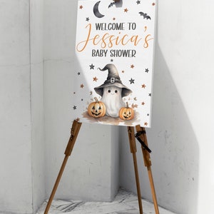 K&ouml;nnte beinhalten: Ein wei&szlig;es Schild mit einem Geist, der einen Hexenhut tr&auml;gt und zwei Jack-o'-Lantern-K&uuml;rbisse h&auml;lt. Auf dem Schild steht "Willkommen zu Jessicas Baby Shower".