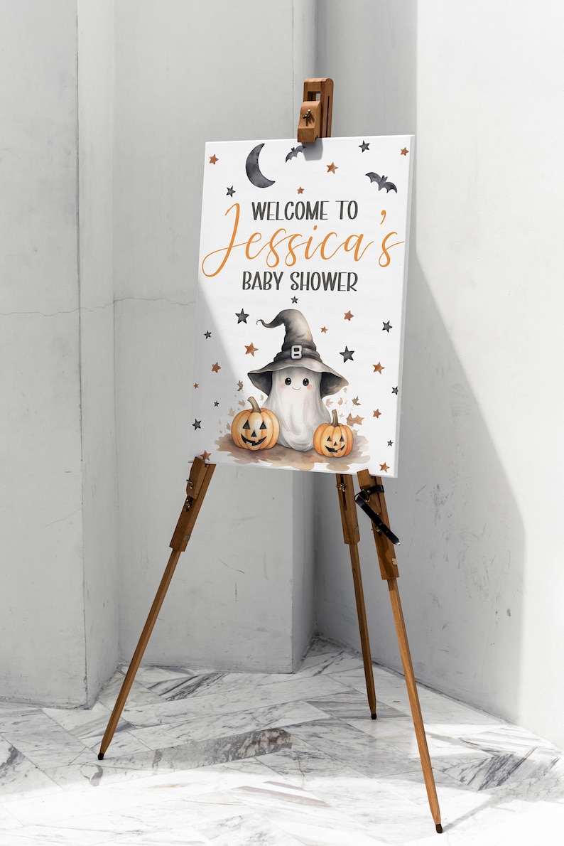 K&ouml;nnte beinhalten: Ein wei&szlig;es Schild mit einem Geist, der einen Hexenhut tr&auml;gt und zwei Jack-o'-Lantern-K&uuml;rbisse h&auml;lt. Auf dem Schild steht "Willkommen zu Jessicas Baby Shower".