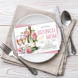 May include: A pink and white invitation card with a watercolor illustration of champagne flutes and a bottle of champagne with pink roses. The text on the card reads "Join us for Brunch with Mom" and includes the date, time, and location of the event.