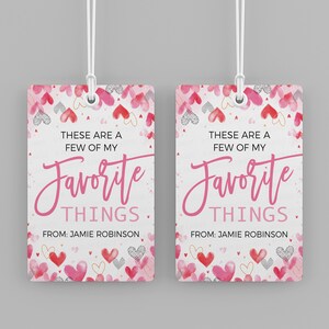 K&ouml;nnte beinhalten: Zwei rosa und wei&szlig;e Geschenkanh&auml;nger mit einem Aquarell-Herz-Muster. Der Text auf den Anh&auml;ngern lautet "Das sind ein paar meiner Lieblingssachen." und "Von: Jamie Robinson".