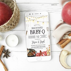 May include: A smartphone displaying a digital invitation for a backyard baby-Q. The invitation features a rustic wood background with string lights, a grill, and a red and white checkered picnic blanket. The text reads "Join us for a Backyard Baby-Q, November 10, 5:00PM, in honor of Jessun & Josoph, 555 Baby Dr,  Crillin, VA 55555".