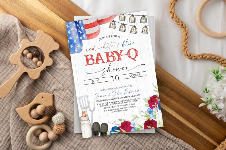 May include: Red, white, and blue baby shower invitation with a watercolor American flag, string lights, and floral accents. The invitation reads "Join us for a red, white & blue baby-q shower" with the date and time of the event.