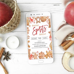 May include: A smartphone displaying a digital invitation for a "Baking Spirits Bright" Christmas cookie decorating party. The invitation features a watercolor illustration of gingerbread cookies, candy canes, and other holiday decorations. The party is hosted by the Robinson family on December 10th at 5:00 PM.