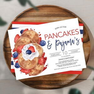 May include: A white invitation card with a watercolor illustration of pancakes topped with whipped cream, strawberries, and blueberries. The text on the card reads "Join us for Pancakes & Pajama's!"  "February 10, 10:00 AM"  "To Celebrate Jamie's Birthday"  "The Robinson's Home"  "555 Pancake Dr | Syrup VA 55555"  "Join us for pancakes & juice"  "Wear your favorite PJs"  "RSVP with Jamie by Jan 1st at 555-555-5555"