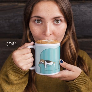 attractive woman taking a sip of foamy latte from a coffee mug that has an image of a sleeping Beagle