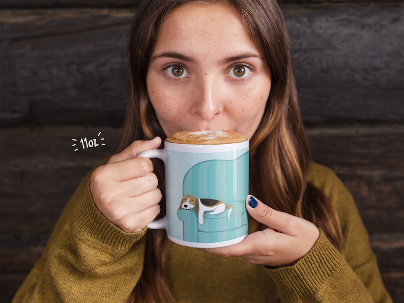 attractive woman taking a sip of foamy latte from a coffee mug that has an image of a sleeping Beagle