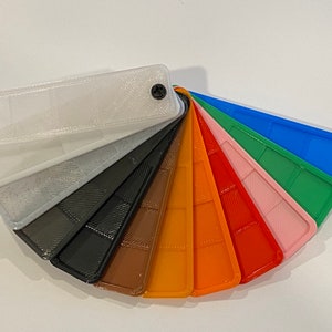 Puede incluir: Una carta de colores en forma de abanico con 10 muestras de pl&aacute;stico diferentes. Las muestras est&aacute;n dispuestas en orden de arco&iacute;ris, comenzando con blanco y terminando con azul. Cada muestra tiene una superficie texturizada.