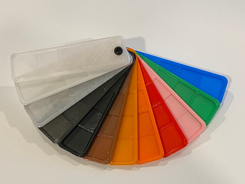 Puede incluir: Una carta de colores en forma de abanico con 10 muestras de pl&aacute;stico diferentes. Las muestras est&aacute;n dispuestas en orden de arco&iacute;ris, comenzando con blanco y terminando con azul. Cada muestra tiene una superficie texturizada.