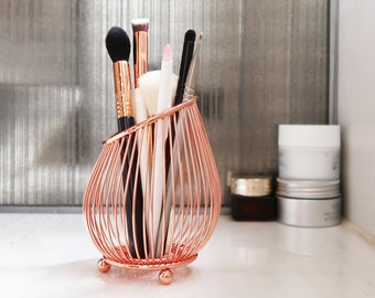 May include: Rose gold wire makeup brush holder with a variety of brushes and applicators inside.