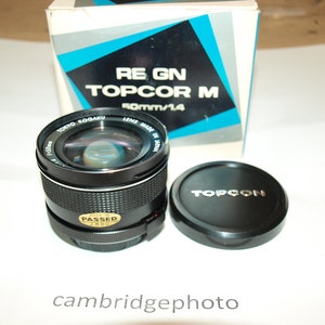 Può includere: Un obiettivo per fotocamera Topcon Topcor M 50mm/1.4 nero con tappo e scatola. L'obiettivo presenta la scritta "TOKYO KOGAKU LENS MADE IN JAPAN" e "PASSED". La scatola riporta la scritta "RE GN TOPCOR M 50mm/1.4".