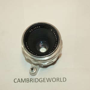 May include: A silver camera lens with black markings. The lens is labeled "C.Z. Jena" and "T Tessar 1:2.8".