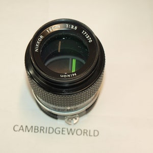 May include: A black Nikon Nikkor 135mm f/3.5 lens with a serial number of 171370. The lens is in focus and the aperture is open.