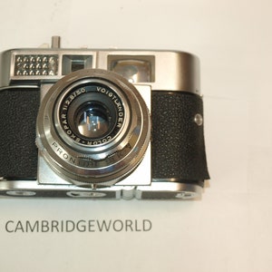 May include: A silver and black 35mm film camera with a Voigtlander Color-Skopar 1:2.8/50 lens. The camera has a black leatherette covering and a silver metal body.