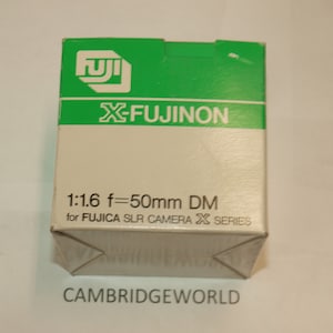 Puede incluir: Una caja blanca con texto verde y un logotipo de Fujifilm. El texto dice "X-Fujinon 1:1.6 f=50mm DM para cámara réflex Fujica X Series".