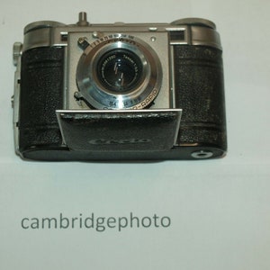 May include: A silver and black 35mm film camera with a lens labeled "TESSAR 1:3.5/50" and "COLOR-RAPID".