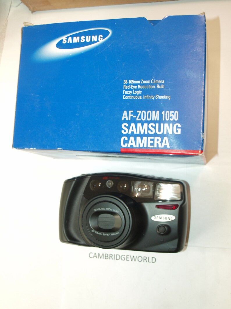 Puede incluir: Una c&aacute;mara Samsung AF-Zoom 1050 negra con un objetivo zoom de 38-105 mm. La c&aacute;mara tiene un flash incorporado y una funci&oacute;n de reducci&oacute;n de ojos rojos. La c&aacute;mara est&aacute; en su caja original azul con texto blanco.
