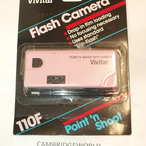 以下が含まれることがあります： オリジナルのパッケージに入ったピンクのビビタ 110F ポイントアンドシュートカメラ。パッケージは黒で、白と赤の文字が書かれている。カメラは、内蔵フラッシュ付きのポイントアンドシュートフィルムカメラです。