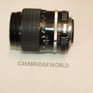 May include: A black camera lens with a silver ring and a black rubber grip. The lens has a depth of field scale and a focus ring.