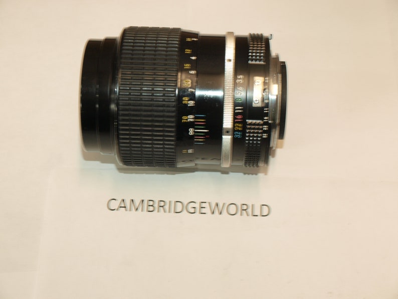 May include: A black camera lens with a silver ring and a black rubber grip. The lens has a depth of field scale and a focus ring.