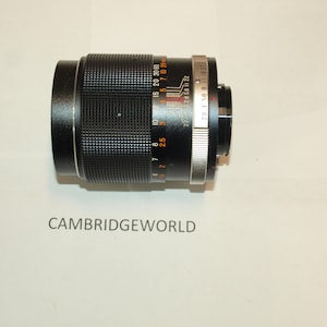 Può includere: Un obiettivo per fotocamera nero con dettagli argentati e segni arancioni. L'obiettivo ha una scala di profondità di campo e segni di apertura. L'obiettivo è contrassegnato con "28 4 56 8 11 16 22" e "28 56 11 22".