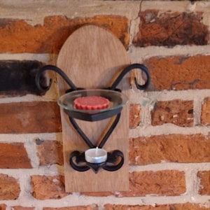 May include: A wall-mounted candle holder with a wooden base and black metal accents. The holder has two candle cups, one for a tealight and one for a larger candle. The holder is mounted on a brick wall.