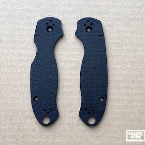 May include: Two black plastic knife scales with a textured surface and multiple holes. The scales are designed for a folding knife.