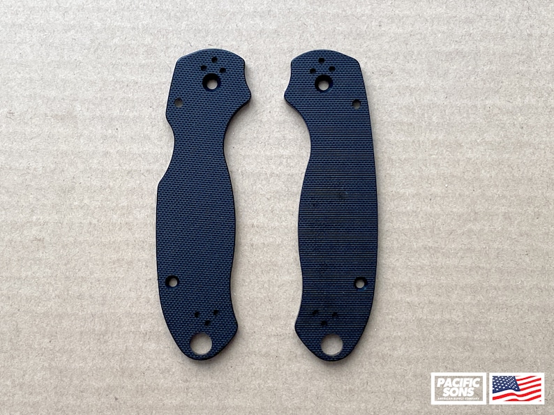 May include: Two black plastic knife scales with a textured surface and multiple holes. The scales are designed for a folding knife.