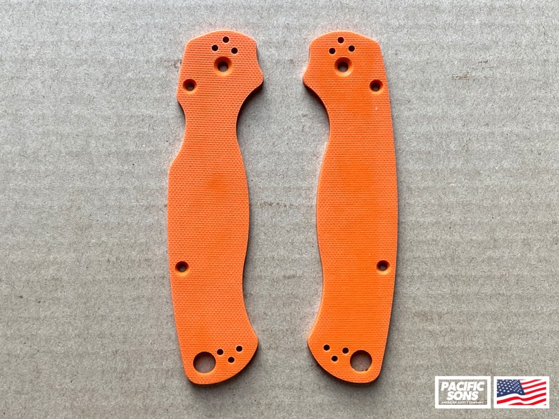 May include: Two orange plastic knife scales with holes for mounting hardware. The scales are textured and have a slightly curved shape.