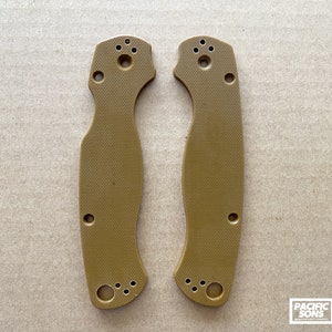 May include: Two tan-colored plastic knife scales with a textured surface and multiple holes. The scales are designed to fit a knife handle.