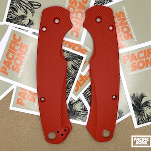 May include: Two red, textured, plastic knife scales with a Pacific Sons logo. The scales have a textured pattern and are designed to fit a knife handle.