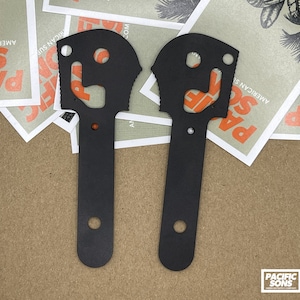 May include: Two black metal tools with a unique design. Each tool has a rounded handle and a variety of cutouts, including a bottle opener, a pry bar, and a wrench.