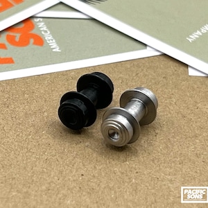 Puede incluir: Dos rodillos metálicos, uno negro y otro plateado, con forma cilíndrica lisa. Los rodillos están diseñados para su uso en un sistema mecánico.