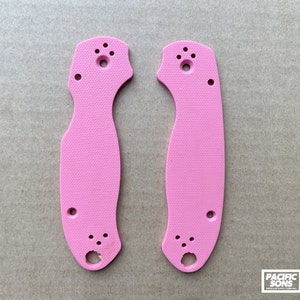 May include: A pair of pink knife scales with a textured surface. The scales have multiple holes for mounting.