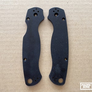 May include: Two black plastic knife scales with a textured surface and multiple holes. The scales are designed for a folding knife.