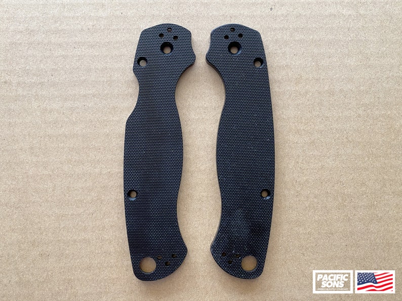 May include: Two black plastic knife scales with a textured surface and multiple holes. The scales are designed for a folding knife.