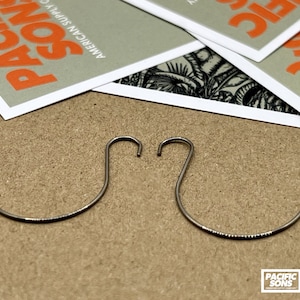 May include: Two silver-colored metal earring hooks. The hooks are curved and have a slight bend at the top. The hooks are isolated on a brown background.