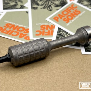 May include: A silver titanium screwdriver with a black tip and a textured grip. The screwdriver is made by Pacific Sons American Supply Company.