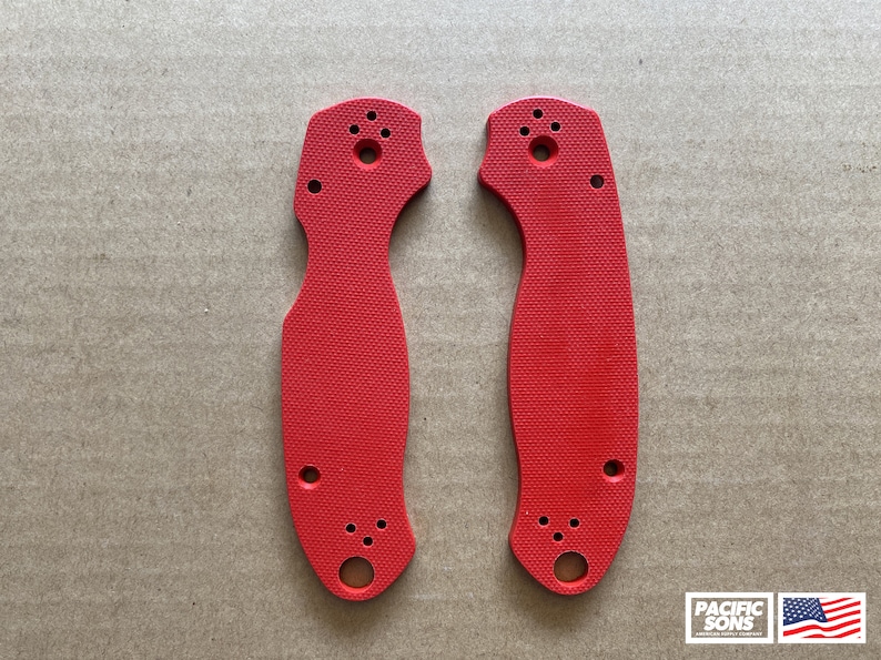 May include: Two red plastic knife scales with holes for mounting hardware. The scales are textured and have a slightly curved shape.
