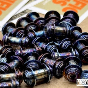 May include: A pile of iridescent metal bolts with a unique color pattern of blues, purples, and bronze. The bolts have a cylindrical shape with a flared head. The Pacific Sons logo and an American flag are visible in the corner.