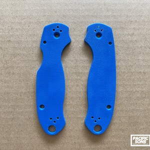 May include: Two blue plastic knife scales with holes for mounting hardware. The scales are textured and have a slightly curved shape.