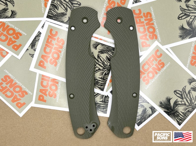 May include: Two green textured knife scales with rounded edges and multiple holes. The scales are on a brown surface with several white squares with the text "Pacific Sons American Supply Company" printed on them.