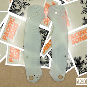 May include: Two white, textured, plastic knife scales. The scales have a pattern of diagonal lines and are designed to fit a knife handle.