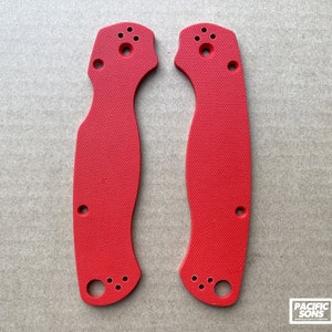May include: Two red plastic knife scales with a textured surface and multiple holes. The scales are designed for a folding knife.