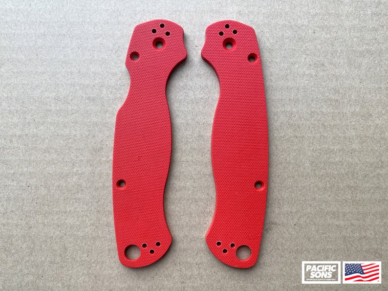 May include: Two red plastic knife scales with a textured surface and multiple holes. The scales are designed for a folding knife.