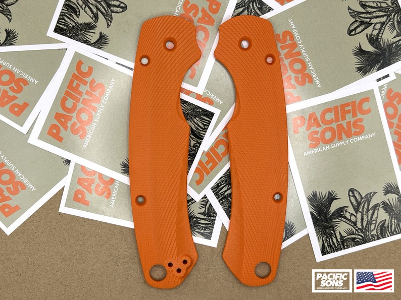 May include: Two orange knife scales with a textured surface. The scales have a rounded shape and are designed to fit a knife handle.