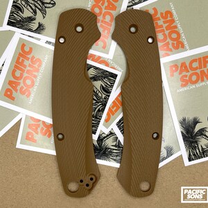 May include: Two brown textured knife scales with rounded edges and multiple holes. The scales are on a brown surface with several white stickers that say "Pacific Sons American Supply Company".