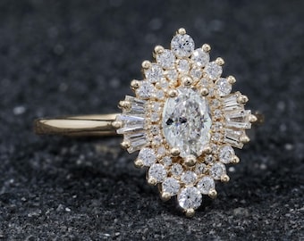 May include: A gold ring featuring a central oval-cut diamond surrounded by a halo of smaller round-cut diamonds and baguette-cut diamonds arranged in a pointed, elongated cluster design. The band is smooth and polished gold metal.