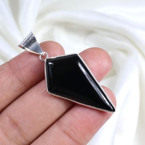 以下が含まれることがあります： 銀色の枠にセットされた黒い宝石のペンダント。ペンダントはダイヤモンド型で、先端が尖っている。