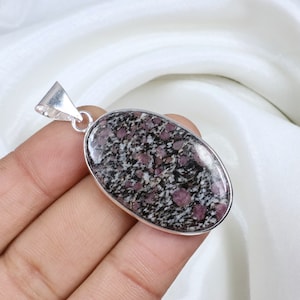 Peut inclure: Pendentif ovale avec une pierre tachetée, gris foncé et rose, sertie dans un cadre en métal argenté. La pierre a une finition polie et brillante. Le pendentif a une bélière argentée pour attacher une chaîne.